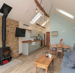 A kitchen area with wooden countertops and a dining table with chairs next to a living space with a couch and a wood burning stove at The Cart Shed in Barwick near Yeovil Somerset