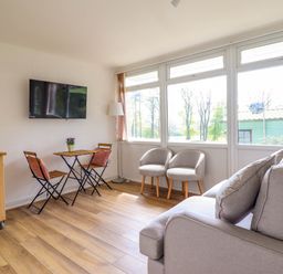 A living room with wooden floor a wall mounted TV two armchairs a small table with two chairs and a sofa at Hill View in Bryncrug near Tywyn