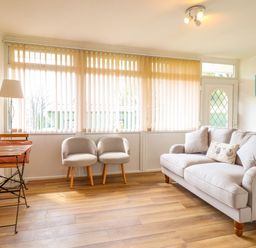 A sitting room with a sofa two chairs a small dining table and vertical blinds on the windows at Hill View in Bryncrug near Tywyn