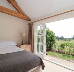 A bedroom with a bed lamp and open doors leading to a garden at Orchard View in Redmary D Abitot near Hartpury