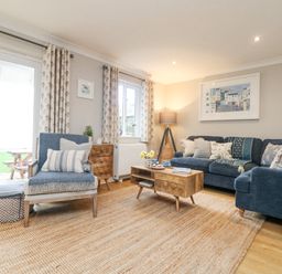A living room with blue upholstered chairs and sofa wooden coffee table and floor lamp at Breeze Cottage in Falmouth