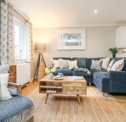 A living room with a blue sofa and armchair a wooden coffee table and a floor lamp at Breeze Cottage in Falmouth