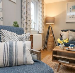 A living room with blue and white pillows on chairs table with flowers and tea set at Breeze Cottage in Falmouth