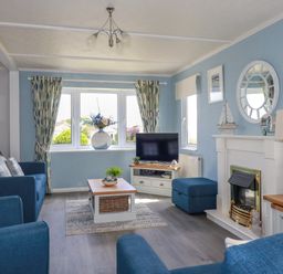 A living room with blue sofas a coffee table a television on a stand and a fireplace at Lowen Lodge in St Merryn near Padstow