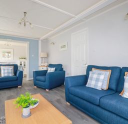 A living room with blue sofas a wooden coffee table with a plant and a lamp on a side table at Lowen Lodge in St Merryn near Padstow