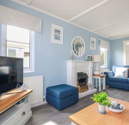 A living room with a blue sofa a fireplace a television and a wooden coffee table at Lowen Lodge in St Merryn near Padstow