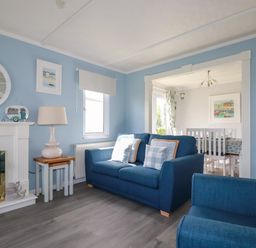 A living room with blue sofas a lamp side table and a fireplace leading to a dining room at Lowen Lodge St Merryn near Padstow