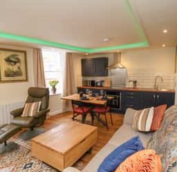 An open plan living room and kitchen with armchair sofa dining table and kitchen appliances at Picadore Two in Scarborough