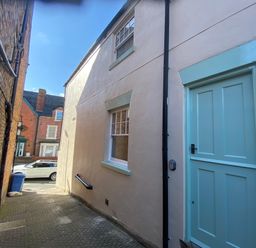 An alleyway with a tan building on the right featuring a blue door and window and a narrow brick building on the left at Picadore Two in Scarborough