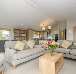 A living room with sofas a wooden coffee table with flowers a dining table and a kitchen area at Lodge 74 at Riviera Bay Coastal Retreat in Brixham