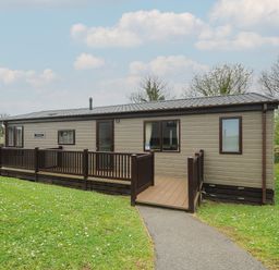 A single story mobile home with a wooden ramp and railing surrounded by grass at Lodge 59 at Riviera Bay Coastal Retreat in Brixham