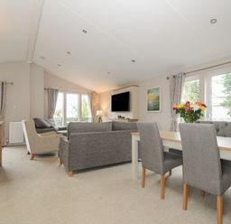 A living room with grey sofas a dining table with chairs and flowers on the table at Lodge 59 at Riviera Bay Coastal Retreat in Brixham