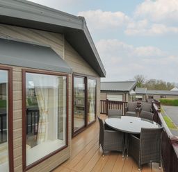 An outdoor balcony with a round glass table and wicker chairs attached to a wooden cabin at Lodge 69 at Riviera Bay Coastal Retreat in Brixham
