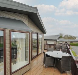 A balcony with a round glass table and six chairs outside a wooden cabin at Lodge 70 at Riviera Bay Coastal Retreat in Brixham