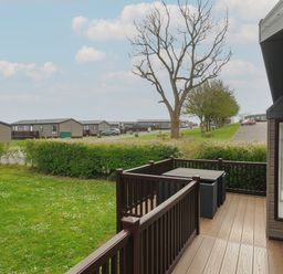 A wooden deck with table and chairs overlooking grass and trees at Lodge 73 at Riviera Bay Coastal Retreat in Brixham