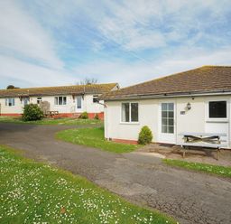 Bungalow houses with picnic tables on lawn and paved pathway under blue sky at Chalet 31 at Landscove Holiday Park in Brixham