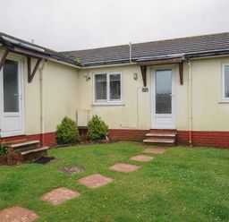 A grassy yard with stepping stones leading to two doors on a single-story building at Chalet 15 at Landscove Holiday Park in Brixham
