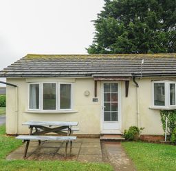 A bungalow with a picnic table on a paved area in front at Chalet 33 at Landscove Holiday Park in Brixham