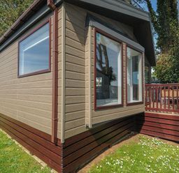 An exterior view of a beige and brown mobile home with large windows and a wooden deck at Lodge 11 at Landscove Holiday Park in Brixham