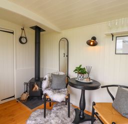 A small room with a wood stove two chairs a round table and a wall shelf at La'al Ling in Penrith