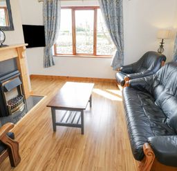 A living room with black leather sofa and armchair a wooden coffee table fireplace and blue floral curtains at Rossaveel Upper in Rossaveel County Galway