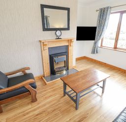 A living room with a wooden coffee table black cushioned wooden armchair fireplace and a window with curtains at Rossaveel Upper in Rossaveel County Galway