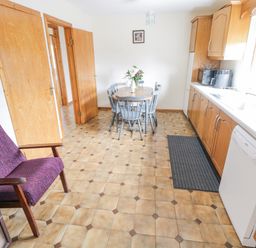 A kitchen with wooden cabinets a dining table with chairs and a dishwasher at Rossaveel Upper in Rossaveel County Galway