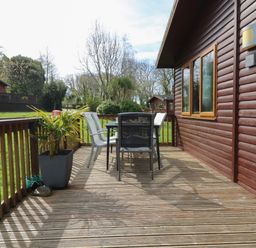 An outdoor wooden deck with a table and chairs next to a cabin at 3 The Glade in St Minver Rock