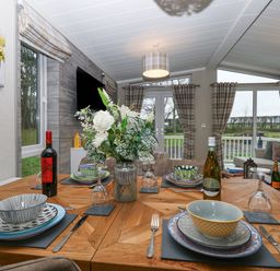 A dining table set with plates bowls wine glasses and bottles in a living area with sofas windows and curtains at Wurzburc in Swaffham