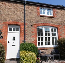 The exterior of a brick house with a white door numbered 7 and white-framed windows with bushes and two black chairs and a table outside at Splash in Weymouth