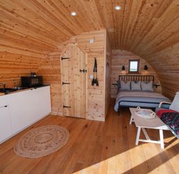 An interior of a wooden pod with a kitchenette a bed a small sofa and a coffee table at Glamping Pod 2 Presence in Lebberston