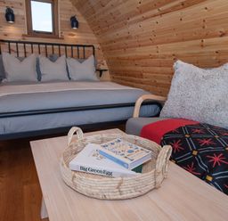 A bedroom with a bed a small table with a basket containing books and a chair with a cushion at Glamping Pod 2 Presence in Lebberston