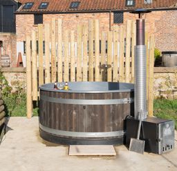 An outdoor wooden hot tub with drinks on the edge and a metal heater beside it at Glamping Pod 3 Harmony Lebberston