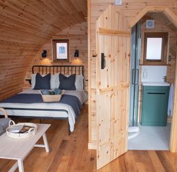 A wooden cabin interior with a bed sofa table and bathroom at Glamping Pod 3 Harmony Lebberston