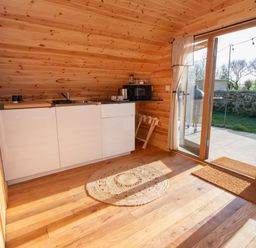A kitchenette with white cabinets a sink a microwave and a window door leading outside at Glamping Pod 3 Harmony in Lebberston