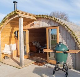 A wooden glamping pod with glass doors open showing a leather sofa inside and a green barbecue outside at Glamping Pod 4 Truce in Lebberston