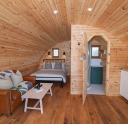 A wooden pod interior with a bed sofa coffee table and an open door to a bathroom at Glamping Pod 4 Truce in Lebberston