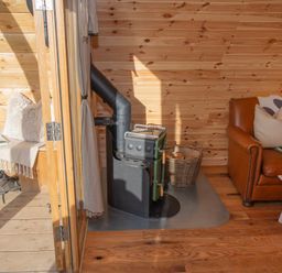A wood-paneled room with a wood stove basket of firewood leather sofa and a porch with bench and boots at Glamping Pod 4 Truce Lebberston