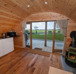 An interior with wooden walls and ceiling a small kitchenette stove and sliding glass doors looking out to a grass field at Glamping Pod 4 Truce in Lebberston