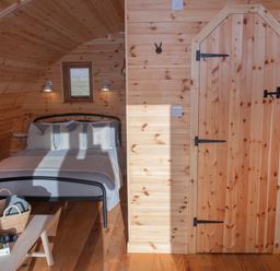 A wooden bedroom with a bed a small window a wooden door and a table with a basket and binoculars at Glamping Pod 5 Shelter in Lebberston
