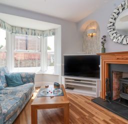 A living room with a floral sofa, wooden coffee table with a board game, TV on a white stand, and a fireplace at Metcalfe House in Compton Dundon