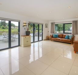 A living room with brown leather sofas blue cushions sliding glass doors and a small cabinet at Timberdyne Brimfield near Woofferton