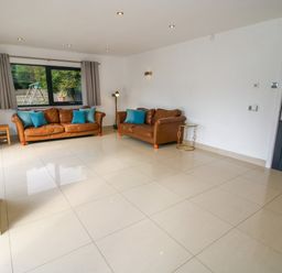 A living room with two brown leather sofas with blue cushions a floor lamp a small round side table and a large window with curtains at Timberdyne in Brimfield near Woofferton