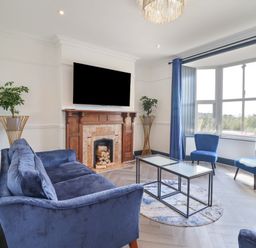 A living room with blue couches and chairs a fireplace with TV above and large window at Gwynfa in Barmouth