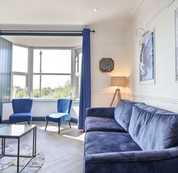 A living room with blue velvet sofa and chairs with floor lamp and wall clock at Gwynfa in Barmouth