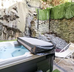 A hot tub with cover and a white lounge chair in an outdoor stone wall area at Gwynfa in Barmouth