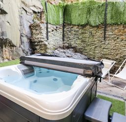 An outdoor hot tub with partially removed cover next to two white deck chairs and stone walls at Gwynfa in Barmouth