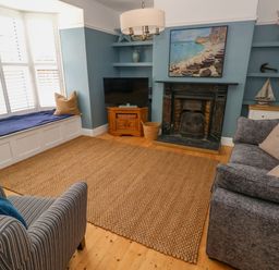 A living room with a fireplace a television a sofa an armchair and a window seat at Suffolk House in Narberth