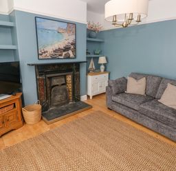 A living room with a gray sofa, a fireplace, a television on a wooden stand, and shelves with decorations at Suffolk House in Narberth