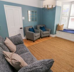 A sitting room with a grey sofa, two armchairs, a wicker rug, and a window seat at Suffolk House in Narberth